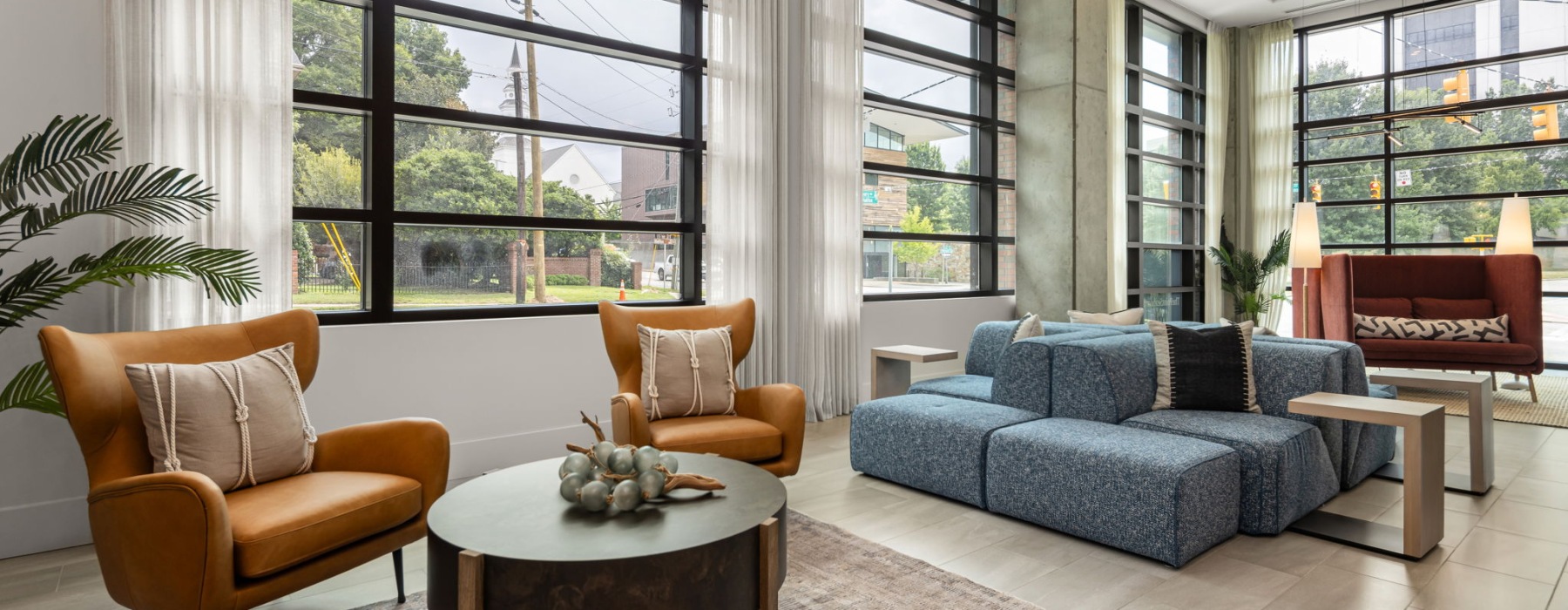 Room with lounge seating and large windows with plants 